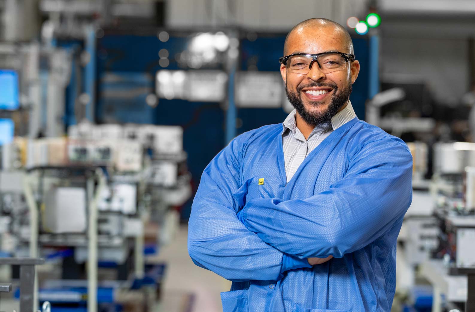Smiling man in blue lab coat and safety glasses standing in a modern manufacturing facility